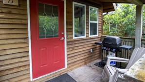 A wooden house with a red door, a barbecue grill, and two windows.