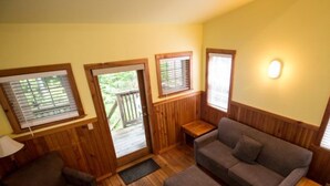 Una habitación acogedora con piso de madera, un sofá gris, una pequeña mesa de madera y una puerta que da a una terraza al aire libre.