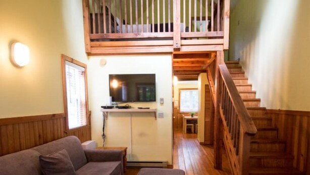 Una sala de estar acogedora con una escalera de madera, un sofá, un televisor y una pequeña cocina.
