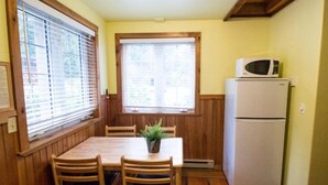 Una cocina compacta con una mesa de comedor, sillas, un refrigerador y una ventana con persianas.