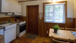 A kitchen with white cabinets, a stove, a sink, and a window with blinds.