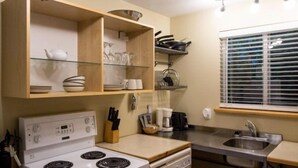 A compact kitchen with a stove, dishwasher, and a window with blinds.