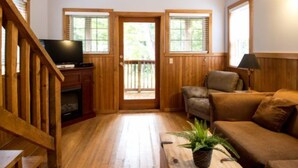 Una sala de estar con piso de madera, un televisor, un sofá, una mesita de centro y una planta en maceta.
