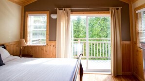 A bedroom with a bed, a nightstand, a window with blinds, and a balcony with a railing.