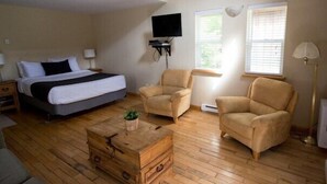 Une chambre à coucher avec un lit, deux fauteuils, une commode en bois, un téléviseur et une fenêtre.