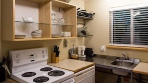 Une cuisine compacte équipée d’une cuisinière, d’un lave-vaisselle et d’une fenêtre avec des stores.