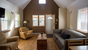 Un salon avec un plafond en pente, un canapé, un fauteuil, une table basse et un téléviseur.