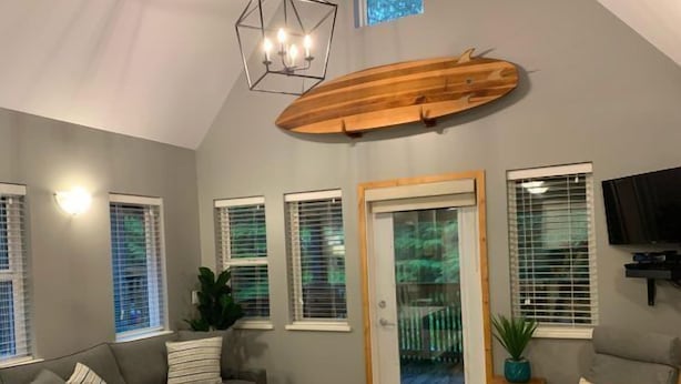 Un salon moderne avec un canapé gris, une table basse en bois, une décoration représentant une planche de surf en bois, un téléviseur et une porte-fenêtre coulissante.