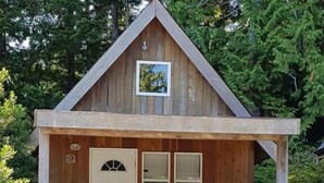 Une petite cabane en bois avec une porte d’entrée, un petit porche doté d’une balustrade et une plaque portant le numéro « 9 ».