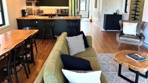 A modern kitchen with a central island, bar stools, a dining table, a leather armchair, and a coffee table.