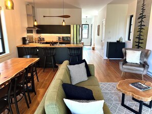 A modern kitchen with a central island, bar stools, a dining table, a leather armchair, and a coffee table.