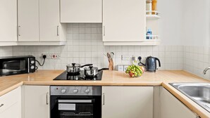 Een moderne keuken met witte kasten, een zwarte oven, een magnetron, een waterkoker en een mand met fruit op het aanrecht.