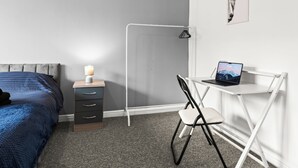 Een slaapkamer met een bed, een bureau met een laptop, een stoel en een nachtkastje met een lamp.