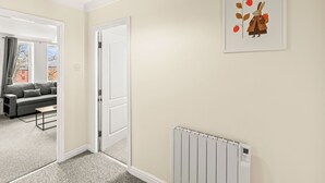 Een kamer met een grijze bank, een witte deur, een radiator en een lijst met een afbeelding aan de muur.