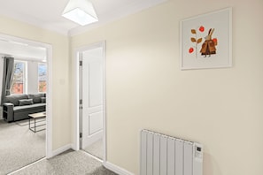 Una habitación con un sofá gris, una puerta blanca, un radiador y un cuadro en la pared.