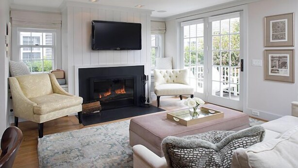 A living room with a fireplace, a television mounted above it, and a large window with a view of greenery. - 2.5 bedroom, 2.5 bathroom (Nantucket)