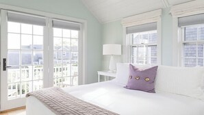 A bedroom with a large bed, a nightstand, a lamp, and a view through a window. - 2.5 bedroom, 2.5 bathroom (Nantucket)