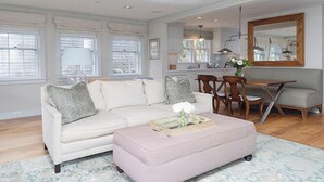 A living room with a white sofa, a small ottoman, and a dining area with wooden chairs and a table. - 2.5 bedroom, 2.5 bathroom (Nantucket)