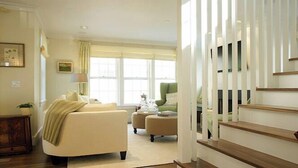A spacious living room with a sofa, a green armchair, and a staircase. - 2.5 bedroom, 2.5 bathroom (Nantucket)