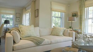 A living room with a white sofa, two pillows, a lamp, and a glass table with bottles. - 2.5 bedroom, 2.5 bathroom (Nantucket)