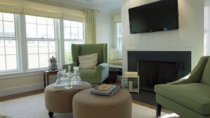 A living room with a green armchair, ottoman, fireplace, flat-screen TV, and large windows. - 2.5 bedroom, 2.5 bathroom (Nantucket)