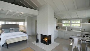 A modern bedroom with a large bed, a fireplace, and a kitchen area with white cabinets and a dining table. - 1 Bedroom, 1 bathroom (Nantucket)