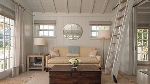 A living room with a beige sofa, a coffee table with a vase, a round mirror, and a bookshelf. - 1 Bedroom, 1 bathroom (Nantucket)