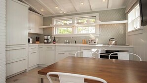 A modern kitchen with white cabinetry, a wooden dining table, and a window with a view of greenery. - 1 Bedroom, 1 bathroom (Nantucket)