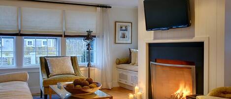 Una sala de estar con chimenea, televisor, sofá, sillón y una mesa con un tazón de bocadillos.