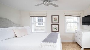 A bedroom with a bed, a ceiling fan, two windows with curtains, a dresser, and two framed pictures on the wall. - 2 bedroom, 2 bathroom (Nantucket)