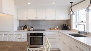 A modern kitchen with white cabinets, a built-in oven, a kettle, and a coffee maker. - 2 bedroom, 2.5 bathroom (Nantucket)