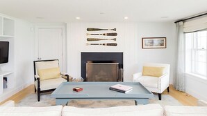 Ein Wohnzimmer mit Kamin, weißen Möbeln und einem Couchtisch mit Büchern und einer Fernbedienung.