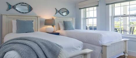 A bedroom with two beds, a ceiling fan, and large windows.