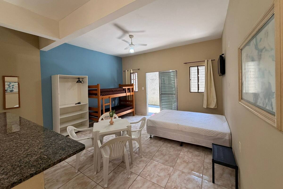 A room with bunk beds, a desk, chairs, a ceiling fan, a window, and a door.