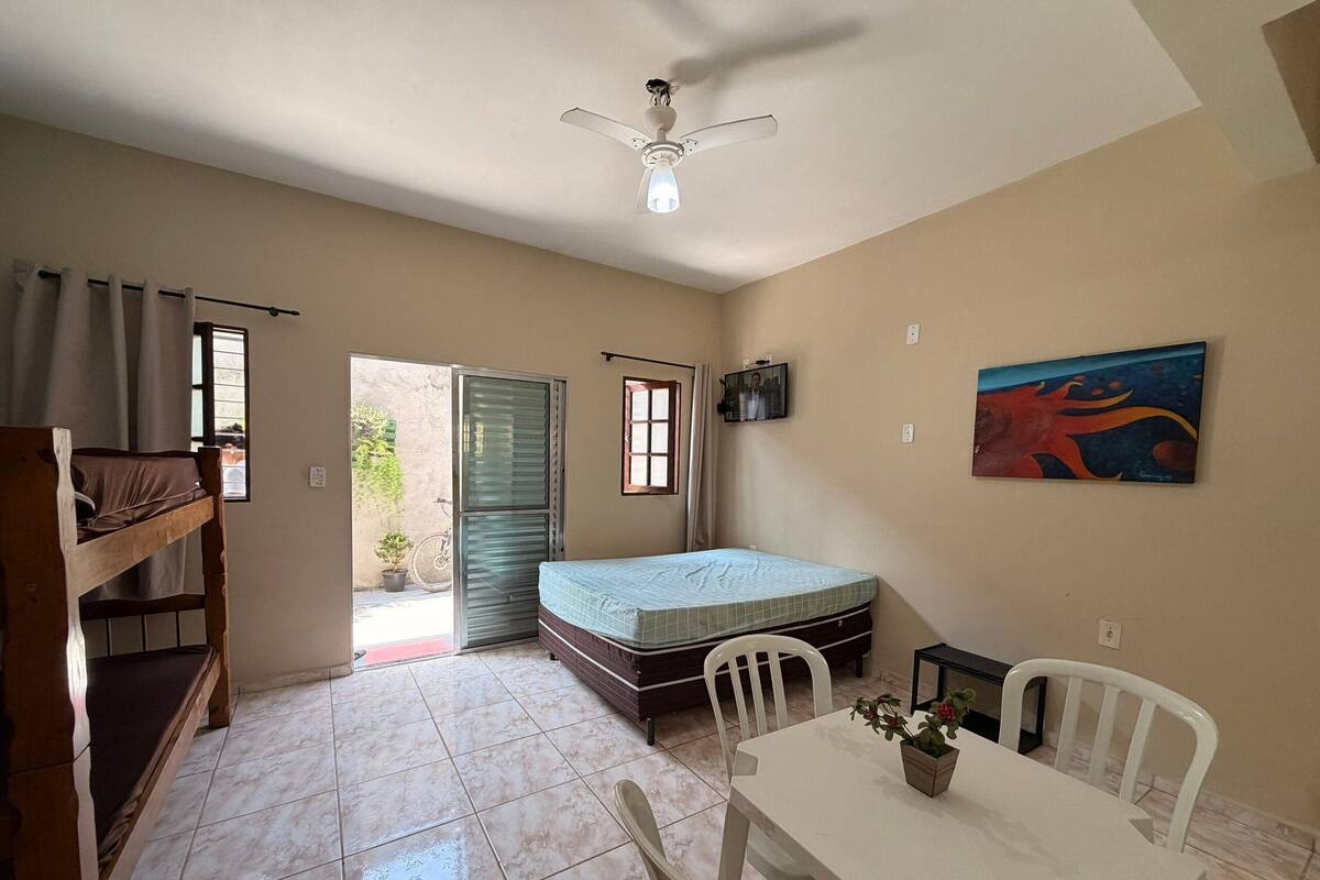 A room with a bunk bed, a single bed, a ceiling fan, a TV, a table with chairs, and a painting on the wall.
