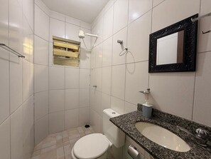 Ein kleines Badezimmer mit Toilette, Waschbecken, Spiegel, Dusche und Fenster.