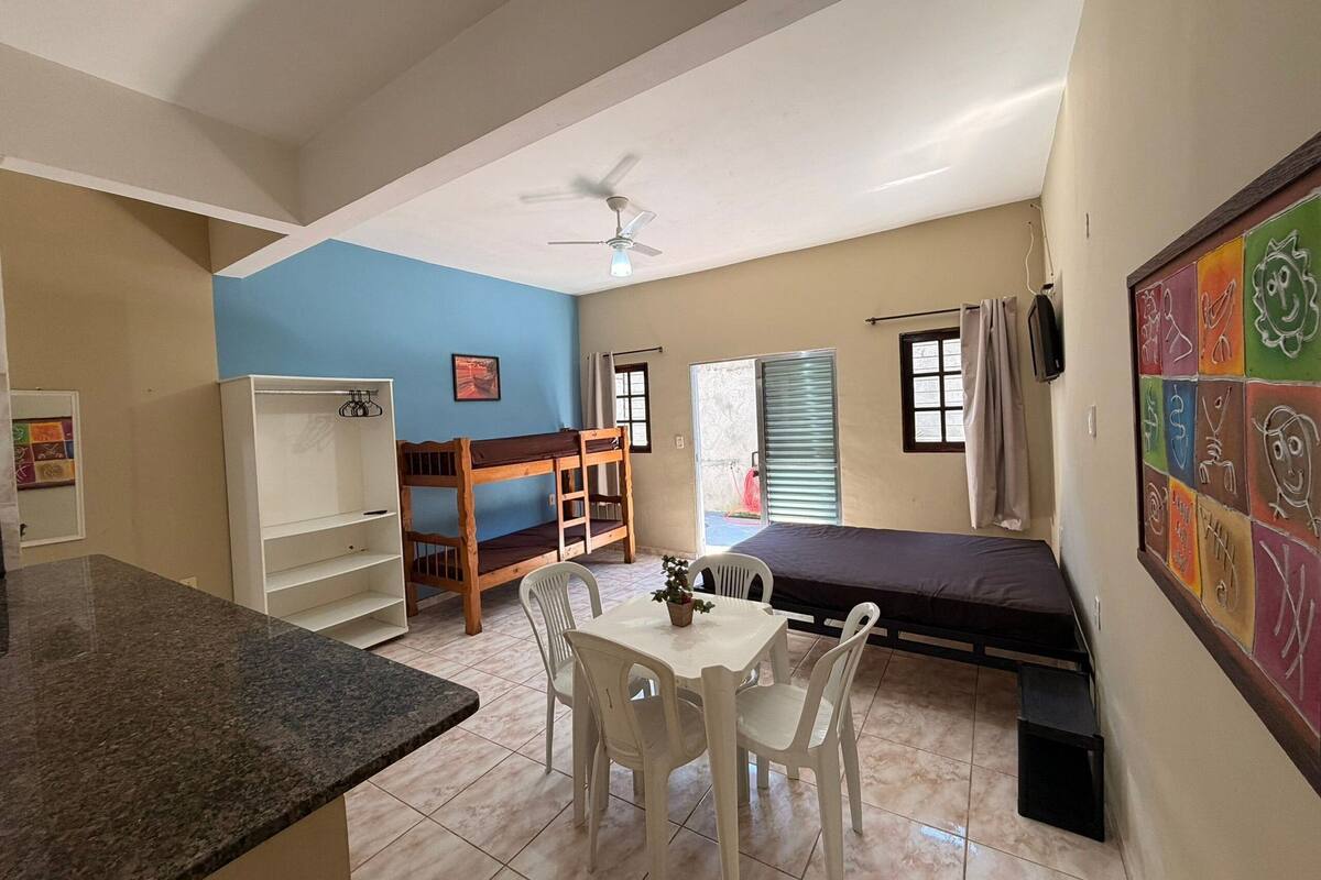 A room with a bunk bed, a desk, a chair, a small table, and a ceiling fan.