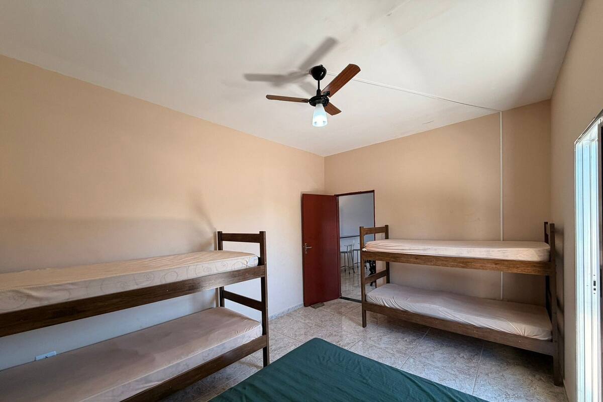 A dormitory room with bunk beds, a ceiling fan, and a door leading to another room.