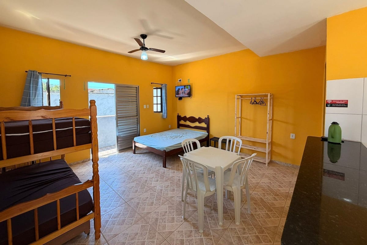 A room with a bed, a table with chairs, a ceiling fan, a TV, and a sign indicating WiFi availability.