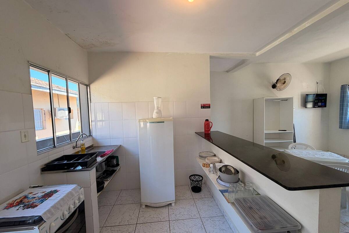 A compact kitchen with a refrigerator, stove, sink, and a window with blinds.