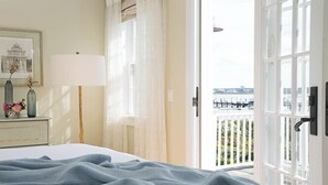 A hotel room with a bed, a nightstand with a lamp, a framed picture, and a view of a balcony with a railing.