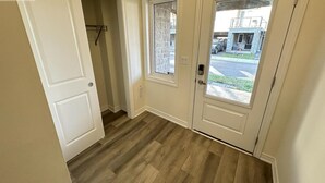 Un pasillo con piso de madera, una puerta blanca y una ventana con vista a la calle y un edificio.