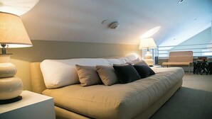 A modern hotel room with a large bed, two bedside tables with lamps, a small table with a chair, and a view of the sky through the ceiling. - 1 Bedroom, 1 bathroom (Nantucket)