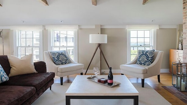 A spacious living room with a modern design, featuring a large window, a floor lamp, and a coffee table with a bottle and glasses. - 1 Bedroom, 1 bathroom (Nantucket)