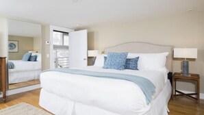 A bedroom with a large bed, two bedside tables with lamps, a mirror, and a view of a balcony. - 1 Bedroom, 1 bathroom (Nantucket)