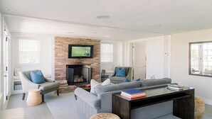 A modern living room with a brick fireplace, a large grey sofa, and a flat-screen TV mounted above it. - 2 bedroom, 2 bathroom (Nantucket)