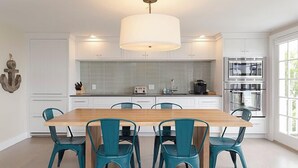 A modern kitchen with white cabinets, a wooden dining table, and teal chairs. - 2 bedroom, 2 bathroom (Nantucket)