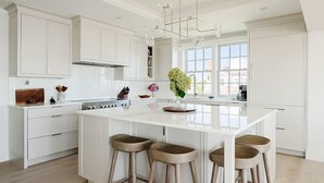 A modern kitchen with white cabinetry, a central island with stools, and a large window providing natural light. - 5 bedroom, 7 bathroom (Nantucket)