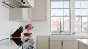 A modern kitchen with white cabinets, a stainless steel stove, a window with a view of buildings, and a vase with flowers on the counter. - 2 bedroom, 2.5 bathroom (Nantucket)