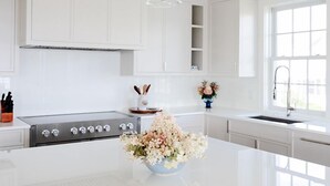 Ett modernt kök med vita skåp, en spis i rostfritt stål och en köksö i mitten, dekorerad med en blomsteruppsättning.